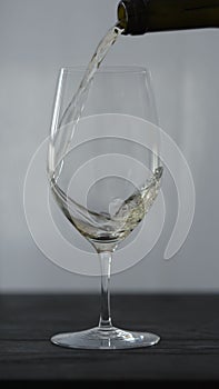 Vertical shot of pour white whine in wine glass on oak table