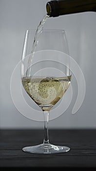 Vertical shot of pour white whine in wine glass on oak table