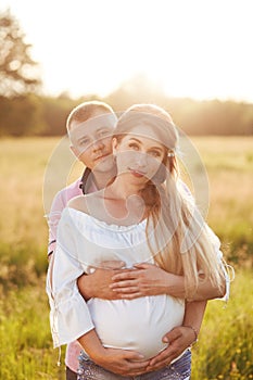 Vertical shot of pregant young woman with her lover stand closely, embrace, anticipate for child, stand together against green mea