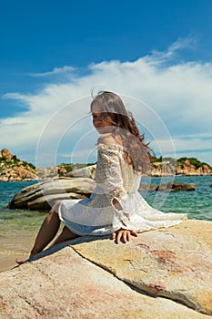 Vertical shot of a pretty Asian girl sitting on rocks near the beach