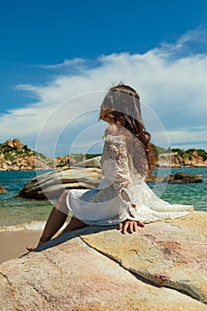 Vertical shot of a pretty Asian girl sitting on rocks near the beach