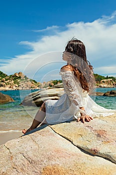 Vertical shot of a pretty Asian girl sitting on rocks near the beach