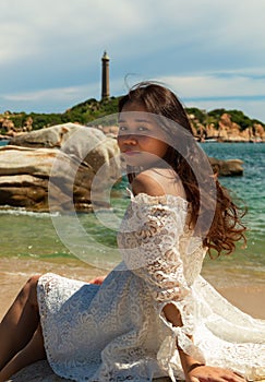 Vertical shot of a pretty Asian girl sitting on rocks near the beach