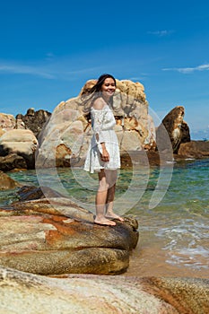 Vertical shot of a pretty Asian girl standing on rocks near the blue ocean in Vietnam