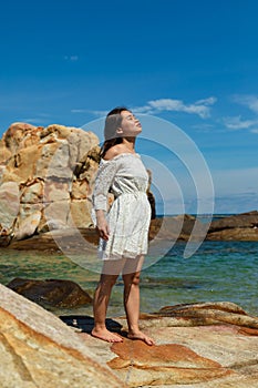 Vertical shot of a pretty Asian girl standing on rocks near the blue ocean in Vietnam
