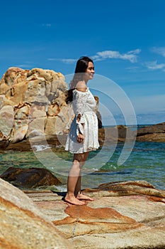 Vertical shot of a pretty Asian girl standing on rocks near the ocean in Vietnam