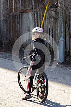 Vertical shot of pretty little girl with dark blond windswept hair sitting on her bicycle