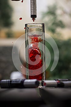 Vertical shot of red ink being poured with a syringe into a glass of water