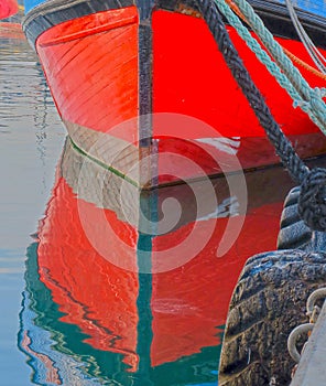 Vertical shot of a red ship reflecting in the sea at the harbor