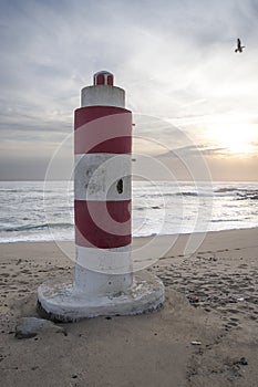 Vertical shot of a red and white striped buoy on the beach