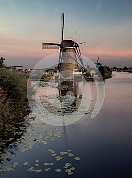 Vertical shot of a river with watermills in the background under cloudy sky at sunrise in Kinderdjik