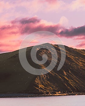 Vertical shot of the rocky hill by the sea under a pink sky with clouds