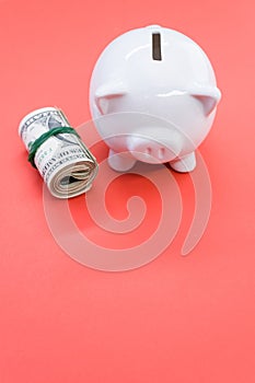 Vertical shot of a roll of dollar bills and a piggy bank on a red surface