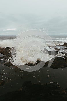 Vertical shot of rough waves crashing against rocks