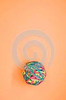 Vertical shot of a rubber ball made out of rubber bands isolated on an orange background