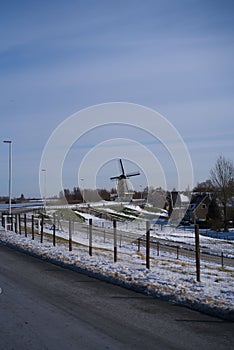 Vertical shot of a rural landscape in winter with a road and an old windmill in the background