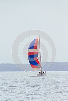 Vertical shot of a sailing boat with a colorful spinnaker