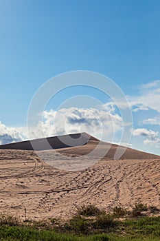 Vertical shot of sand dune under cloudy blue sky
