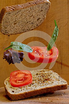 Vertical shot of sandwich bread slices, tomato slices and lettuce on wooden background