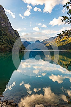 Vertical shot of a scenic fjord near Briksdal Glacier with refrection of blue cloudy sky, Norway