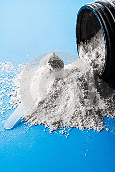 Vertical shot of a scoop of creatine powder on a scattered powder on a blue surface