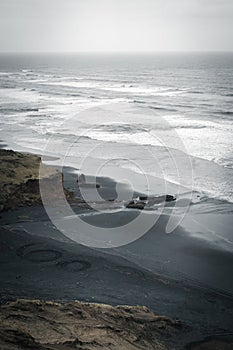 Vertical shot of the sea and a black-sand beach on a cloudy day