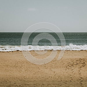 Vertical shot of a sea waves crashing on sandy seashore under a blue sky