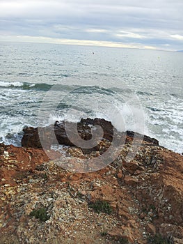 Vertical shot of the seawater splashing on the mossy rocks