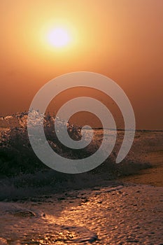 Vertical shot of seawaves covering the coastline in the sunset