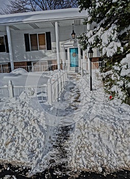 Vertical shot of a shoveled walkway to a turquoise door in front of a house after a big snowstorm