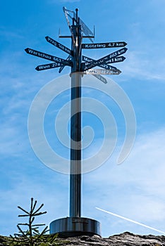 Vertical shot of a signpost indicating the directions and distances under a blue sky with clouds.