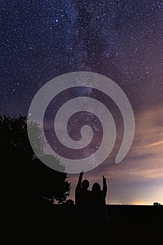Vertical shot of silhouettes of a couple pointing at the milky way in the night sky