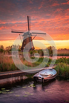 Vertical shot of a small boat in a lake and a mill in the background under the cloudy sunset sky