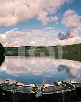 Vertical shot of small boats in the shore of a lake with reflection of the sky in the  water surface