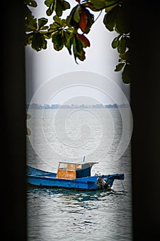 Vertical shot of a small motor boat in the water seen through a crack with greenery above