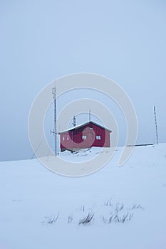 Vertical shot of a small, red cottage on the snowy hill