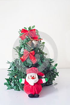 Vertical shot of a small santa toy in front of a Christmas tree on white surface