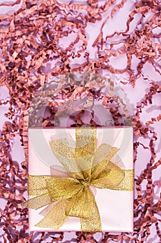 Vertical shot of a small wrapped gift box with golden bow on pink background with decorative straw