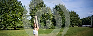 Vertical shot of smiling korean woman doing tree yoga asana, stretching on rubber mat in park, exercising