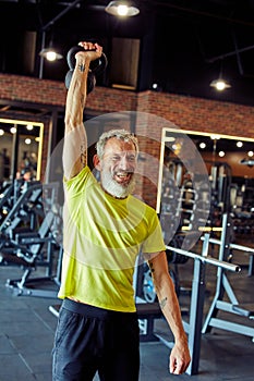 Vertical shot of a smiling mature caucasian man in sportswear exercising with dumbbells at gym