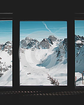 Vertical shot of the snow covered mountains captured through a window