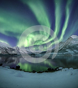 Vertical shot of the snow covered mountains under the beautiful northern lights in the sky