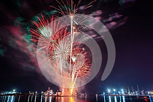 Vertical shot of a Spectacular night sky with an array of fireworks exploding over a body of water