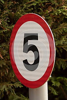 Vertical shot of a speed limit sign with 5 inside a red circle. Vertical