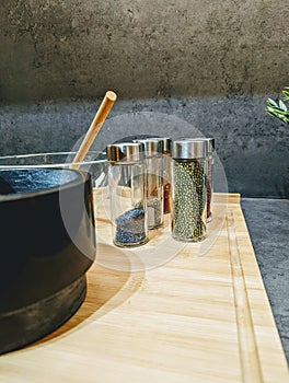 Vertical shot of spice jars next to bowls on wooden board in the kitchen