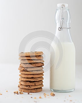 Vertical shot of a stack of chocolate chip cookies beside a bottle of milk on white background