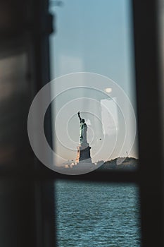 Vertical shot of the statue of liberty behind a boat window