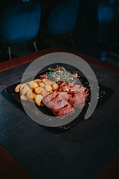 Vertical shot of steaks, baked potato, and a greeny leaf salad on a black plate