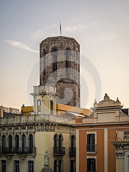 Vertical shot of a stone tower behind the buildings at La Rambla, Barcelona