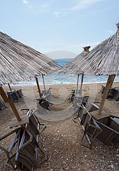 Vertical shot of straw beach umbrellas and sunloungers near a sea under a blue sky